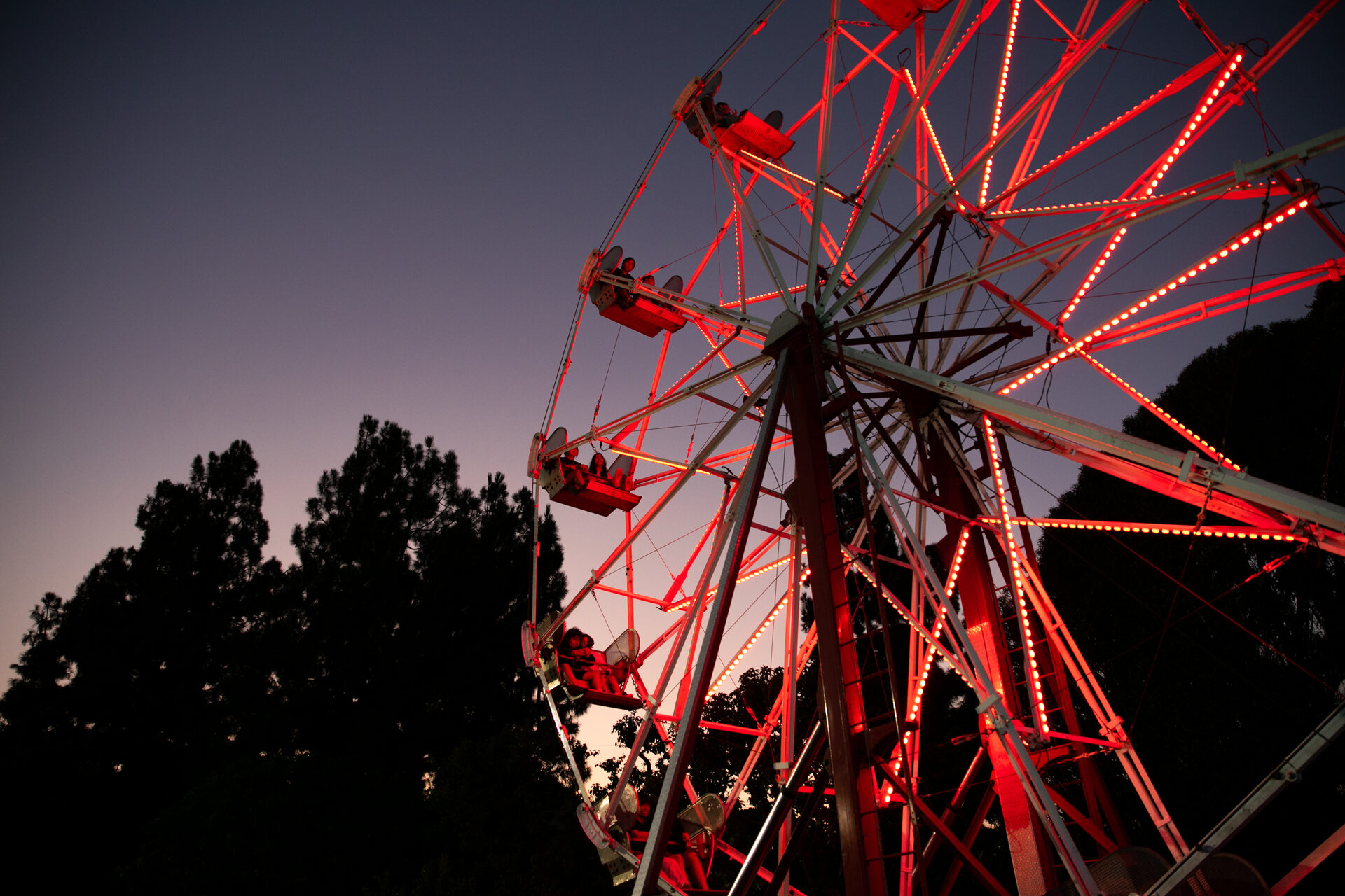 A ferris wheel lit in red against a purple dusk sky, with silhouetted trees